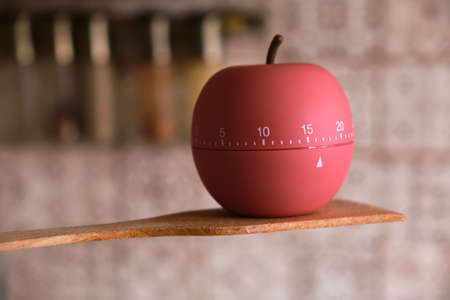 Kitchen timer shaped a apple stands on wooden spatula for cooking or baking in the kitchen, counting...
