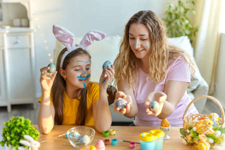 Mother and her daughter playing with painted eggs. Happy family preparing for Easter. Cute little...