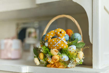 Basket decorated with flowers, eggs, feathers and a toy bunny with colorful pastel eggs on the kitchen cabinet table. Spring easter composition.の写真素材
