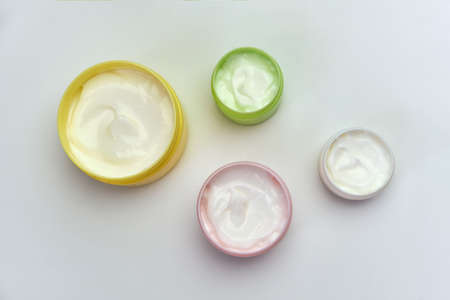 Set of opened multi-colored jars with white cosmetic cream for face and body on a white background,