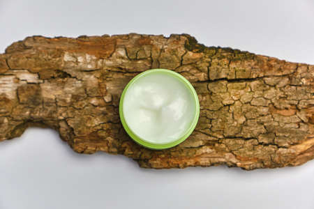 Face cream in green jar on tree bark, white background. Natural cosmetics concept. Top veiw