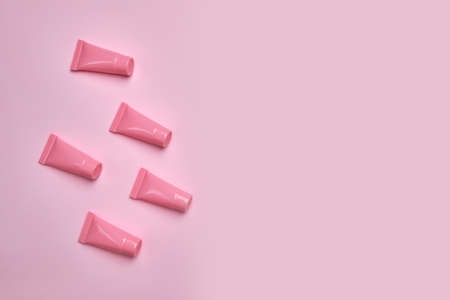 Blank pink cosmetic tubes on pink background. Packaging cream containers design. Flat lay, top view.の写真素材