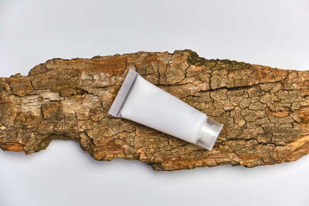 Facial moisturizer cream or facial cleanser in white plastic tube on tree bark, white background. Natural cosmetics concept.の写真素材