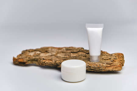 Facial moisturizer cream or facial cleanser in white plastic tube and jar on tree bark, white background. Natural cosmetics concept.の写真素材