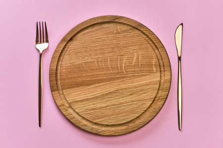 Vintage wooden plate and cutlery on the pink background. Copy space. Flat-lay, top view.