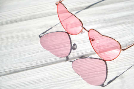 Trendy sunlight summer concept made with heart sunglasses on white wooden table. Minimal summer time concept. Hard shadows.の写真素材