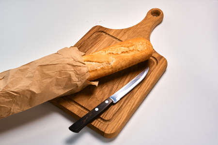 Fresh baguette partly sliced and bread knife on a light backgroundの写真素材