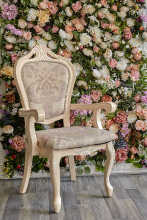 beautiful stylish chair stands against a decorative wall made of multi-colored flower buds. Floral...