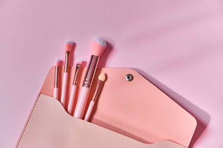 Make up brushes spilling out of a beige cosmetics bag on pastel pink background. Top view. Flat lay. Beauty concept. pink color background, close up view, copy space.の写真素材