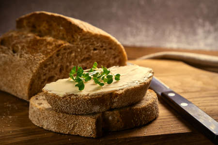 Artisan sliced toast bread with butter and with microgreen broccoli on wooden cutting board with...