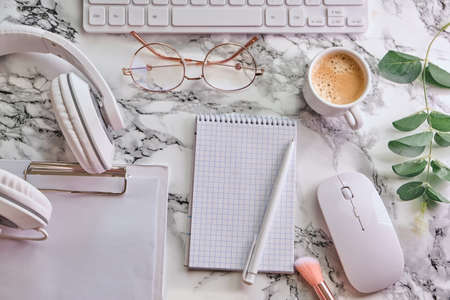 Workplace mockup with notebook, glasses, headphones and make up accessories on white marble background top view. Feminine working style concept.の写真素材