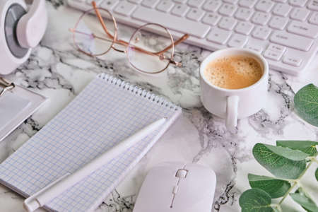 Workplace mockup with notebook, glasses, headphones and make up accessories on white marble background top view. Feminine working style concept.の写真素材