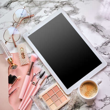 Flat lay composition with tablet and makeup products, coffee and eyeglasses for woman on marble deskの写真素材