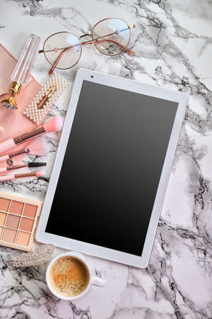 Flat lay composition with tablet and makeup products, coffee and eyeglasses for woman on marble deskの写真素材