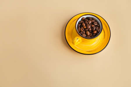 Arabica coffee beans in a bright designer yellow cup with saucer pastel beige paper table. top view, copy spaceの写真素材