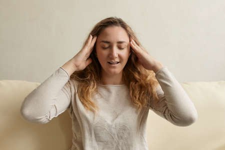 Stressed woman calming down relieving headache emotional stress relief, nervous young woman meditating massaging temples doing breathing exercises on the sofa indoorの写真素材