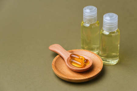 Omega 3 capsules in the wooden spoon on green background, and two bottles of extract, copy space for your design. Cod liver oil capsules on the table. Healthy life style concept.の写真素材