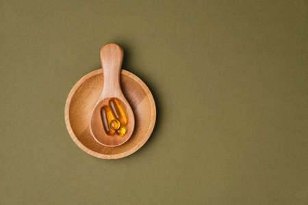 Omega 3 capsules in the wooden spoon on green background, copy space for your design. Cod liver oil capsules on the table. Healthy life style concept.の写真素材