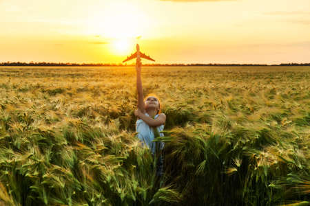 Little girl holding airplane toy during running in the green wheat field during summer day, on sunsetの写真素材