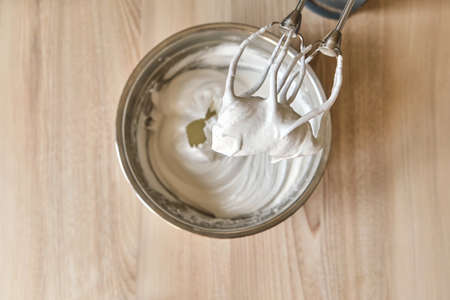 Whipped egg whites and other ingredients for cream or as an ingredient for baking on wooden table,...