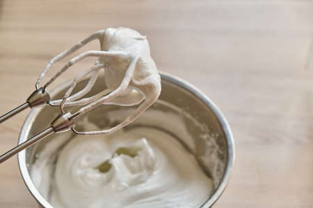Whipped egg whites and other ingredients for cream or as an ingredient for baking on wooden table,...