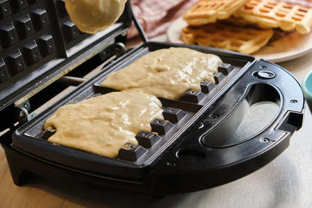 Liquid dough poured waffle iron machine to prepare sweat Belgian waffle dessert. Close up shot.