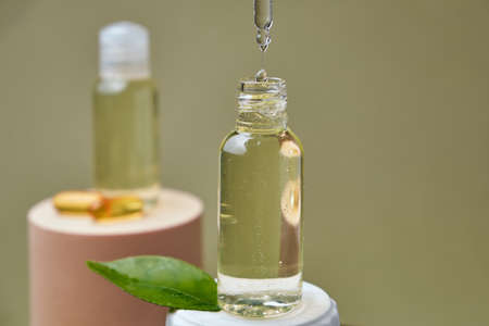 A drop of citrus oil close-up macro drips from a pipette into a bottle on a green background