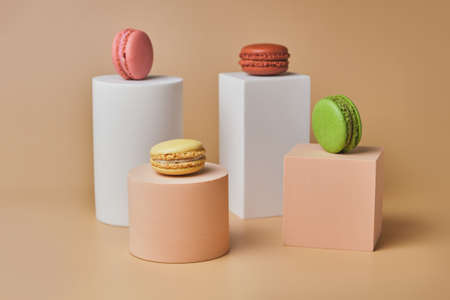 French Colorful Macarons on trendy geometric pedestals on a beige background