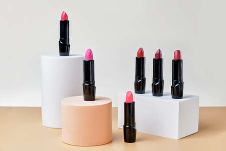 Set of open lipsticks on trendy pedestals, an unbranded presentation of cosmetics on a light beige background. Mockup for the presentation of cosmetics.