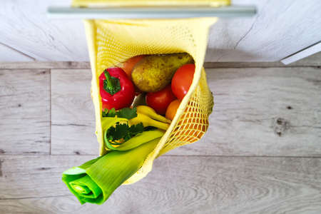 Yellow string shopping bag with vegetables and fruits hanging on a hook in the kitchen