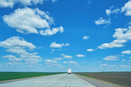 Rural landscape with concrete road and truck far away in motion. Green fields in the background....