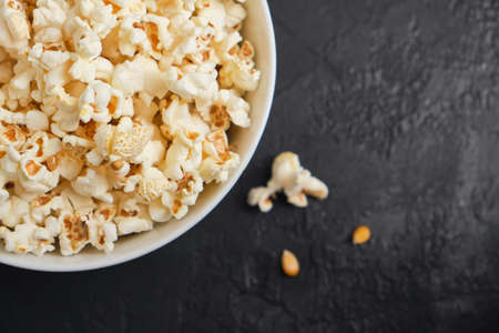 Close up delicious fresh homemade popcorn in a glass bowl on dark background. Snack for watching...