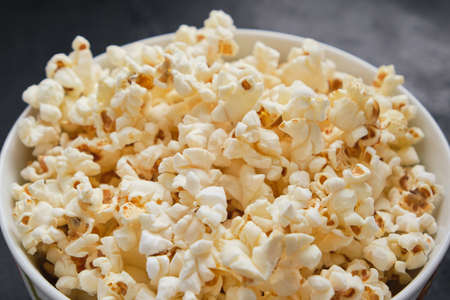 Close up delicious fresh homemade popcorn in a glass bowl on dark background. Snack for watching...