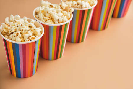 Salted popcorn in small striped paper cups on a beige background. Snack concept for watching movies or a treat for the holidays. Top view, copy spaceの写真素材