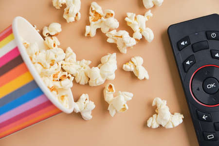 bucket of popcorn, tv remote on beige background. Leisure and entertainment concept. Top view
