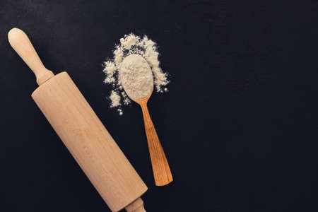 Wheat flour in a wooden spoon with rolling pin over Baking background for your design. on a black slate background. Top view, selective focusの写真素材
