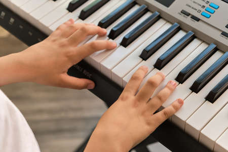 Selective focus of kid's fingers playing the piano. There are musical instrument for concert or learning music. Close up hand of child musician playing the pianoの写真素材