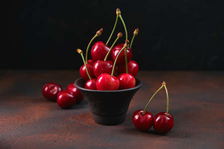 Composition of sweet cherries in a black earthenware bowl on a dark background with water drops....