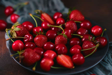 Fresh organic summer mix of strawberry and sweet cherry in round stone plate on dark textured background. Top view, still life, dark moody. Summer raw berries for healthy diet. Food lifestyleの写真素材