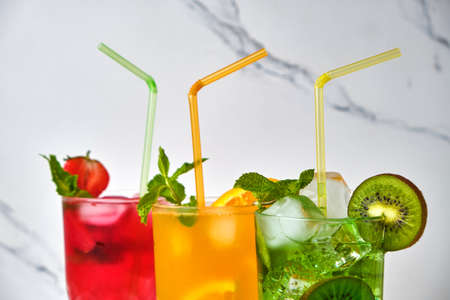 mix of three bright colored delicious cold lemonade carafes of kiwi and orange and strawberry with mint on light background, close upの写真素材