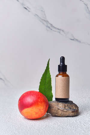 dropper bottle with empty label with a cosmetic serum. Natural cosmetic product. Glass bottle with a product for women's face skincare on a stone stand with fruit peach.の写真素材