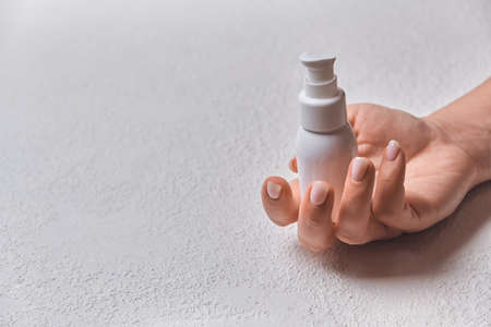 Hand of caucasian young woman holding bottle of body cream over white background with copy spaceの写真素材