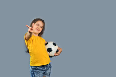 FFan sport girl player hold soccer ball celebrating, happy smiling kid in yellow t-shirt on gray background, shows the gesture of victory, free text copy spaceの写真素材