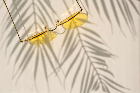 Summer flat lay with yellow sunglasses on water background with shadows of palm leaves and copy space. Concept of summer hot day on the beach.の写真素材