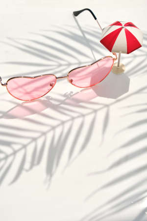 Pink women's sunglasses on white water background with floral palm shadow and toy umbrella. Minimal fashion lifestyle background.の写真素材