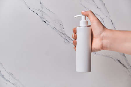 Hand of caucasian young woman holding bottle of body cream over white backgroundの写真素材