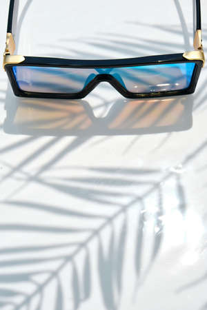 Stylish Sunglasses with mirrored glasses lie on a water background. The shadow of a palm tree. leisure, travel and entertainment concept with copy spaceの写真素材