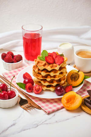 Healthy Breakfast set with Belgian waffles with strawberries, apricots, cherries, juice and a cup of black coffee and bitter chocolate on white stone table backgroundの写真素材