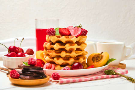 Healthy Breakfast set with Belgian waffles with strawberries, apricots, cherries, juice and a cup of black coffee and bitter chocolate on white stone table backgroundの写真素材