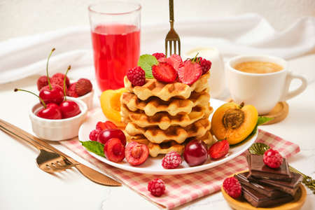 Healthy Breakfast set with Belgian waffles with strawberries, apricots, cherries, juice and a cup of black coffee and bitter chocolate on white stone table backgroundの写真素材